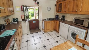 A compact kitchen with wooden cabinets, a microwave, a dishwasher, and a sink. - Horseshoe Cottage (Newquay)