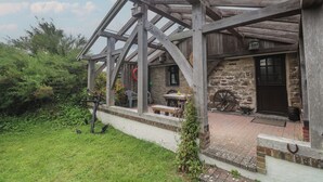 A rustic stone building with a wooden porch and a wheelbarrow. - Horseshoe Cottage (Newquay)