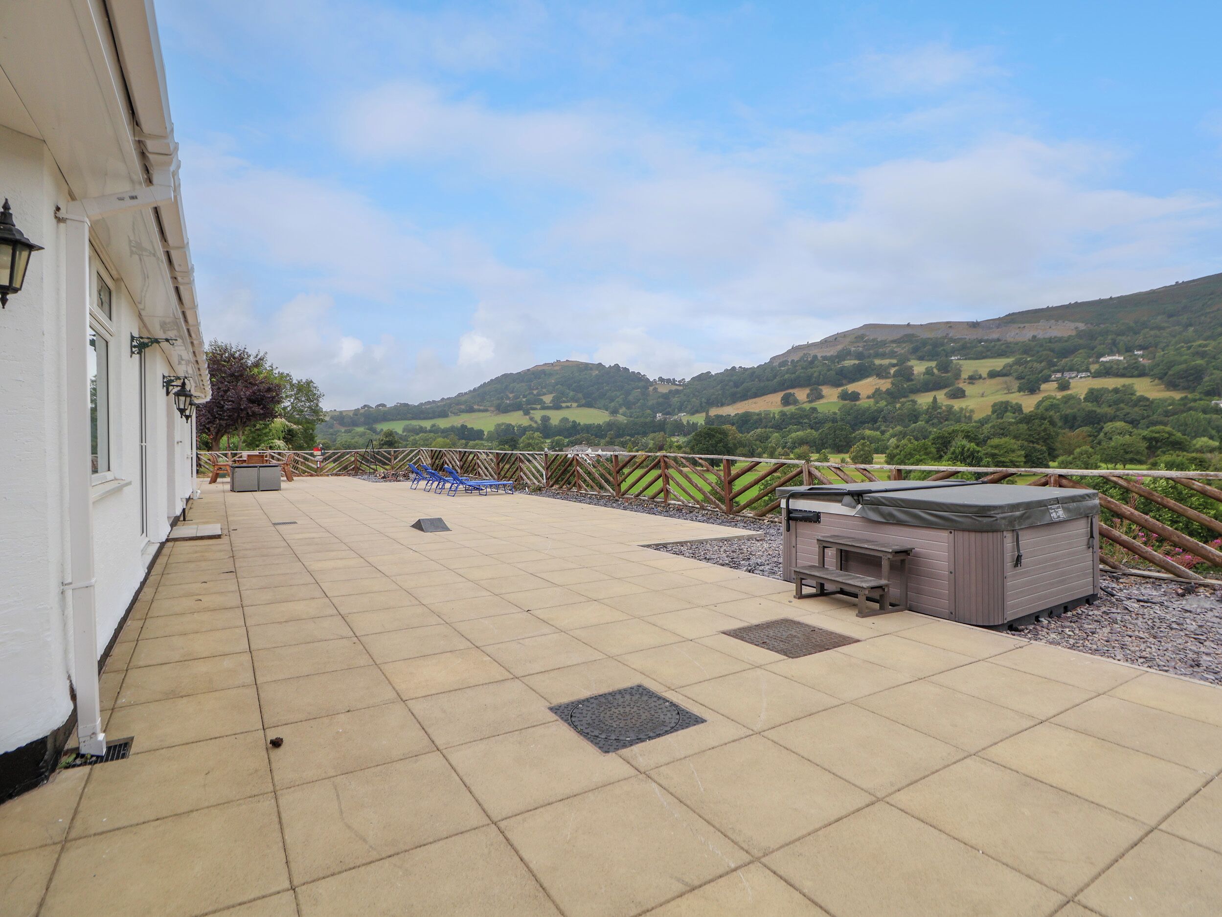 A patio with a view of rolling hills, a barbecue grill, and a covered seating area.