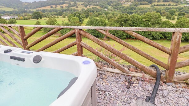 A hot tub with a view of rolling hills and a wooden fence. - The Willows (Llangollen)