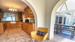 A spacious kitchen with wooden cabinets, a yellow armchair, and a dining area with a view. - The Willows (Llangollen)