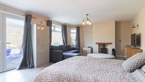 A spacious bedroom with a large bed, a sofa, and a TV. There is a sliding door leading to a balcony with outdoor seating. - The Willows (Llangollen)