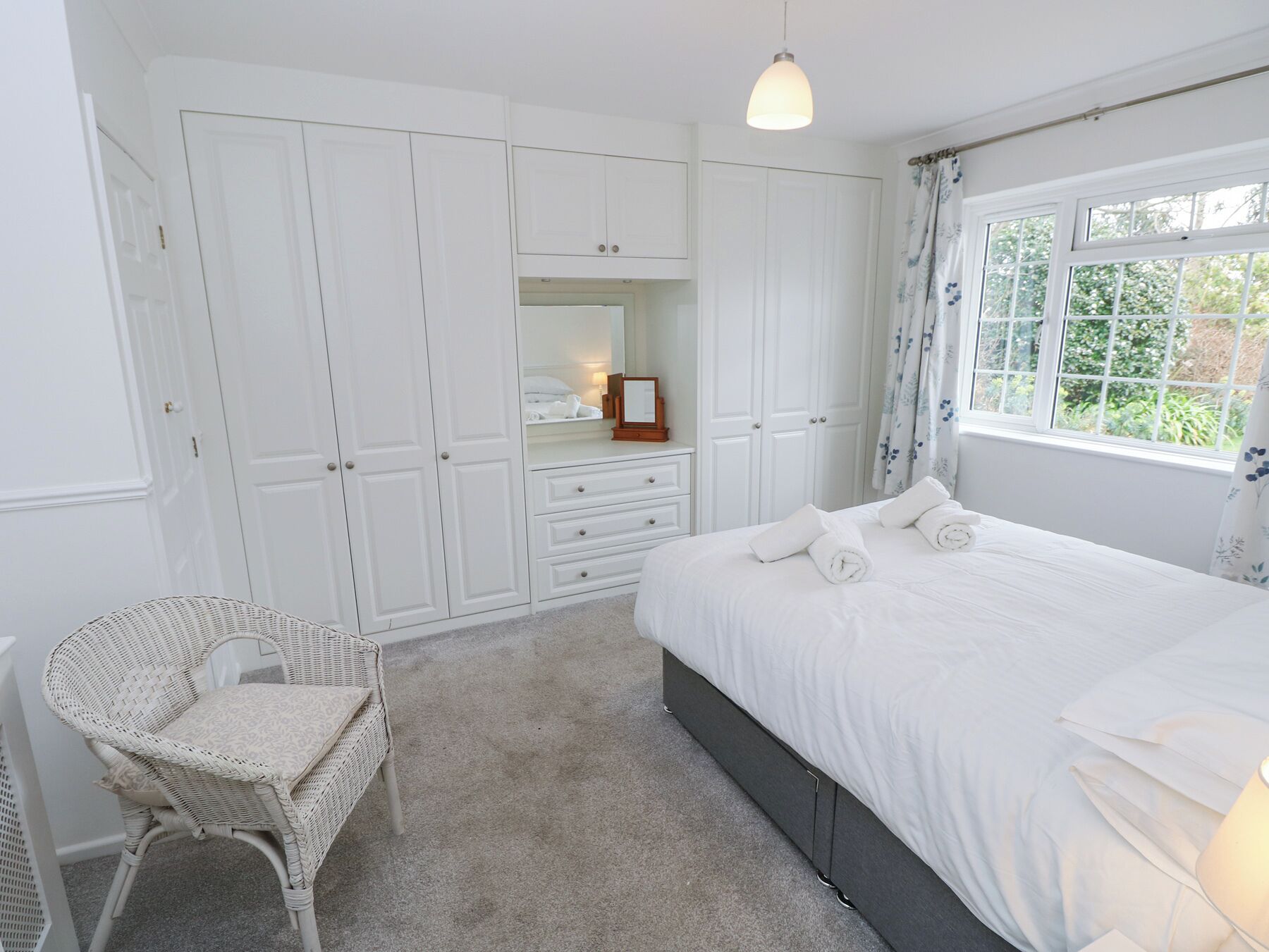 A bedroom with a large bed, a chair, a wardrobe, and a window.