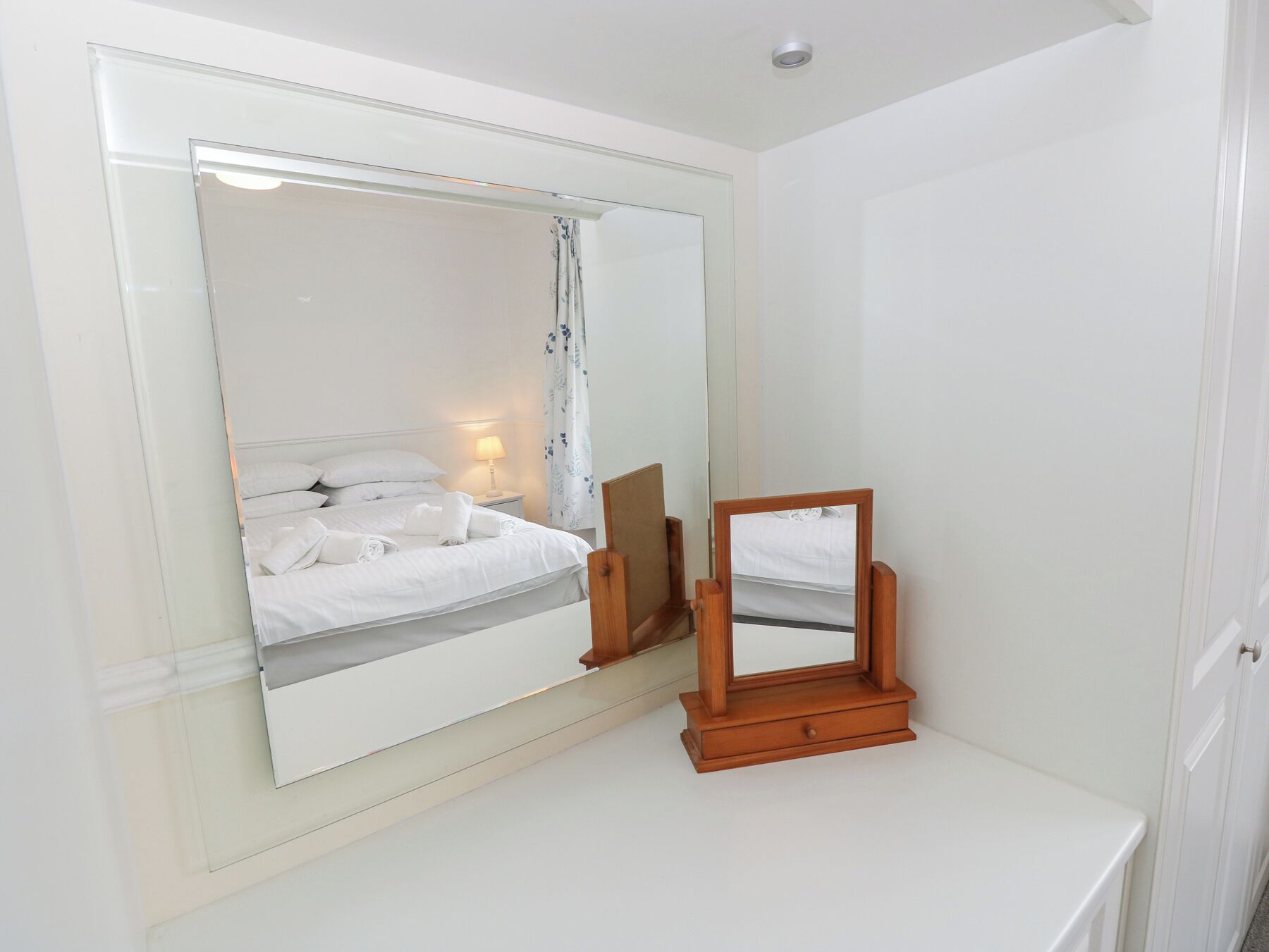 Une chambre à coucher avec un grand miroir, une table de chevet et un lit recouvert de linge de maison blanc.