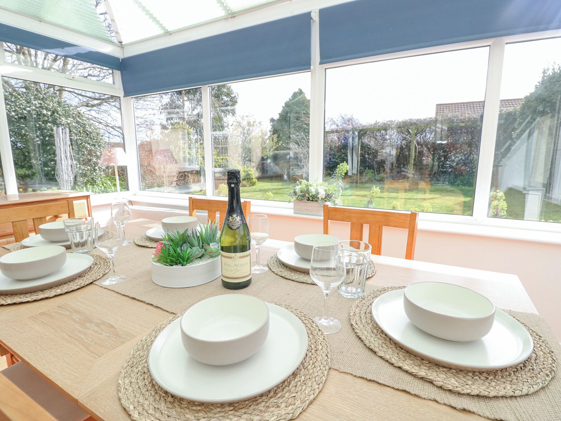 A dining table set for six with white plates, glasses, and a bottle of Pol Acker wine.