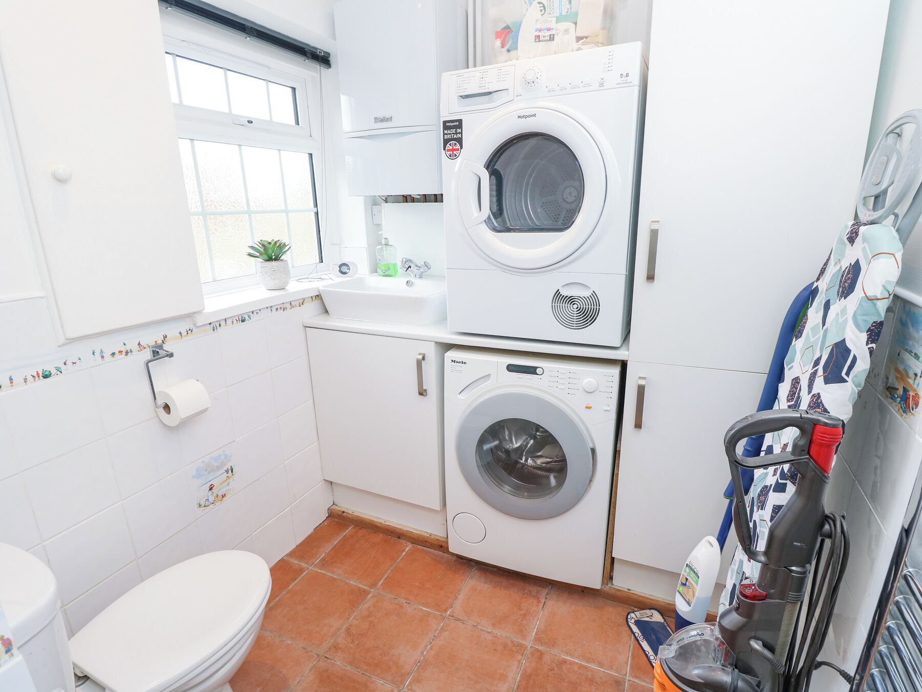 A compact laundry room with two stacked washing machines, a sink, and a toilet.