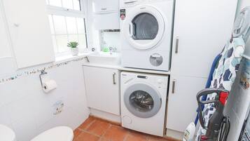 A compact laundry room with two stacked washing machines, a sink, and a toilet.