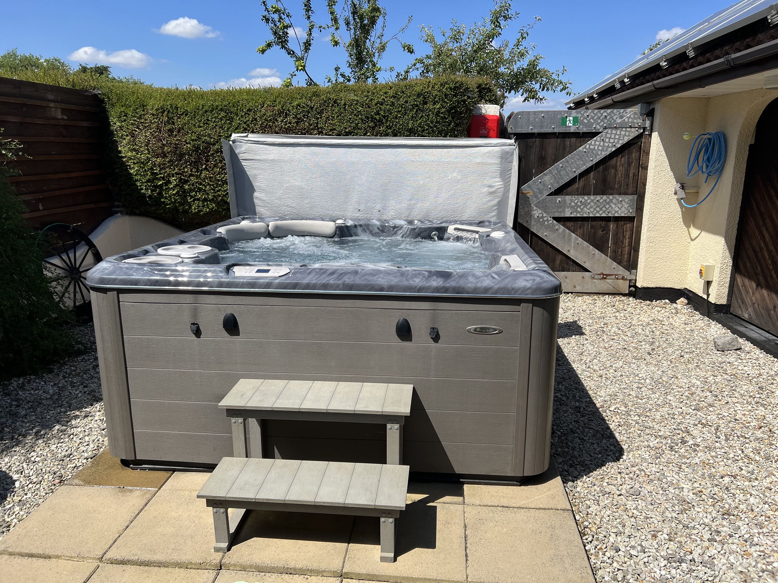 A hot tub with a control panel, a small step-up platform, and a wooden deck.