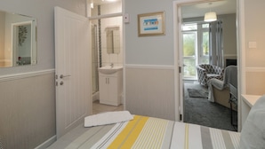 A hotel room with a bed, a bathroom with a sink and mirror, and a view of the outside. - Flat 2, Big Tree Holiday Flats (Paignton)