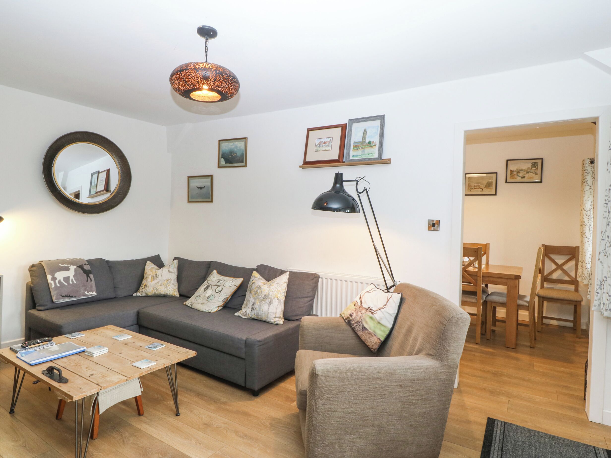 A living room with a sofa, coffee table, and a lamp. There are framed pictures on the wall and a mirror above the sofa.