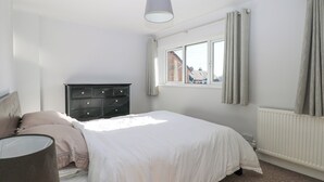 Une chambre à coucher avec un lit, une commode, une fenêtre avec des rideaux et un radiateur.