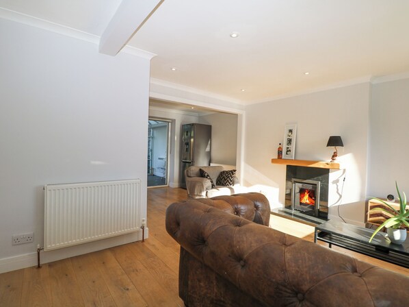 A modern living room with a fireplace, leather sofa, and a view into the kitchen. - 7 Daltons Place (Arundel)