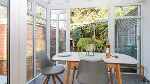 Une véranda avec une table et des chaises, de grandes fenêtres et une plante en pot.
