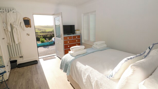 A bedroom with a bed, a dresser, a TV, and a view of the outdoors. - The Hollybush (Kilgetty)