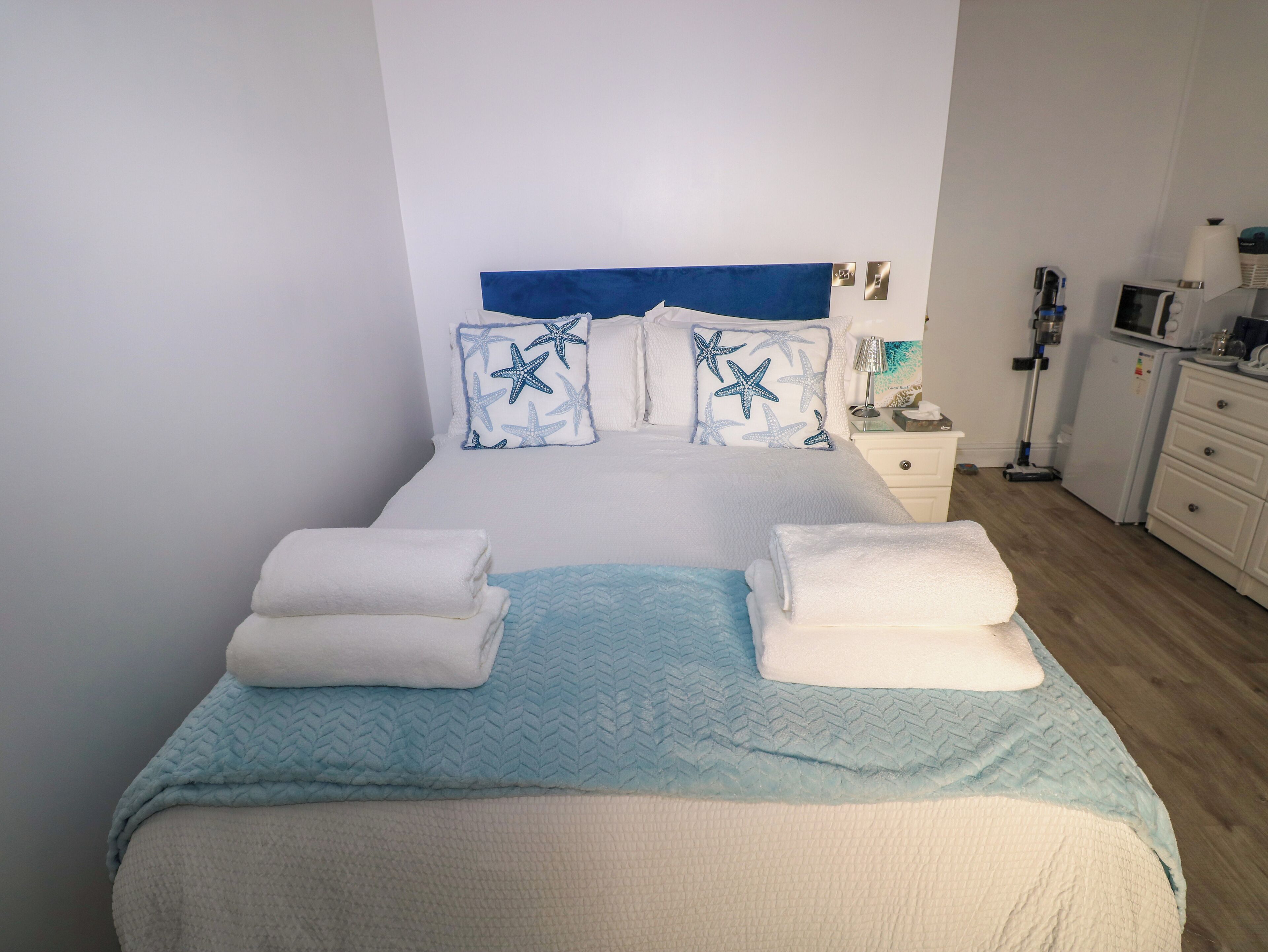 A neatly made bed with star-patterned pillows, a blue quilt, and two folded towels.