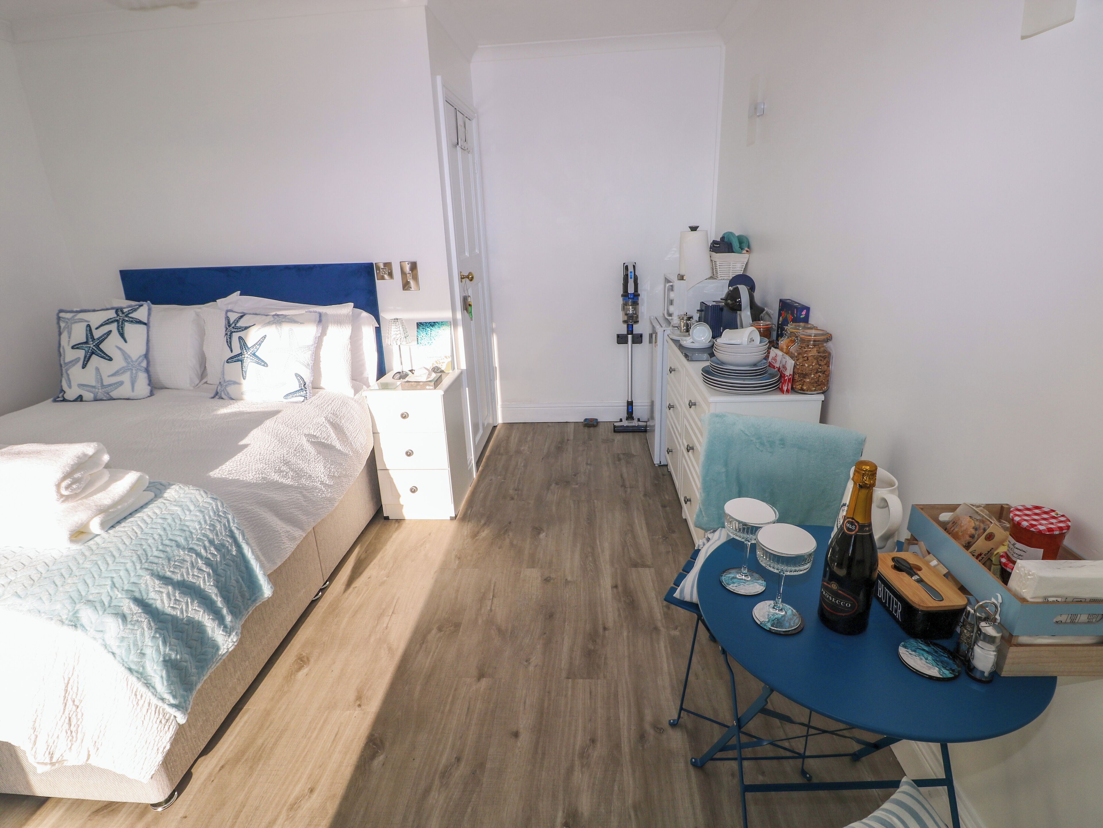 Une chambre à coucher avec un lit, une table de chevet et une petite table sur laquelle se trouvent une bouteille et des verres.