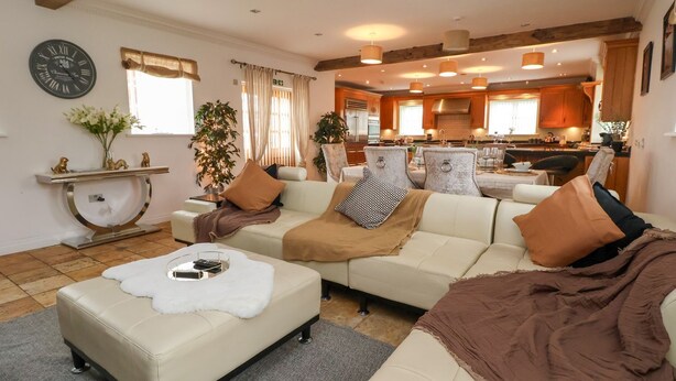 A spacious living room with a sofa, ottoman, and a dining area in the background. - The Wing (Wrexham)