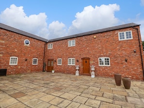 A brick building with a courtyard, featuring a central door, multiple windows, and potted plants.