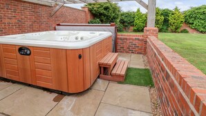 A hot tub with wooden steps and a brick wall backdrop. - The Wing (Wrexham)