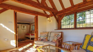 A cozy living room with a sofa, a glass coffee table, and a wooden chair. There is a window with a view of greenery outside. - New House Farm (Robertsbridge)