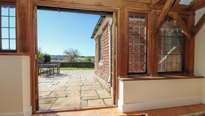 A room with a large open door leading to a patio area with stone flooring and a view of the countryside. - New House Farm (Robertsbridge)