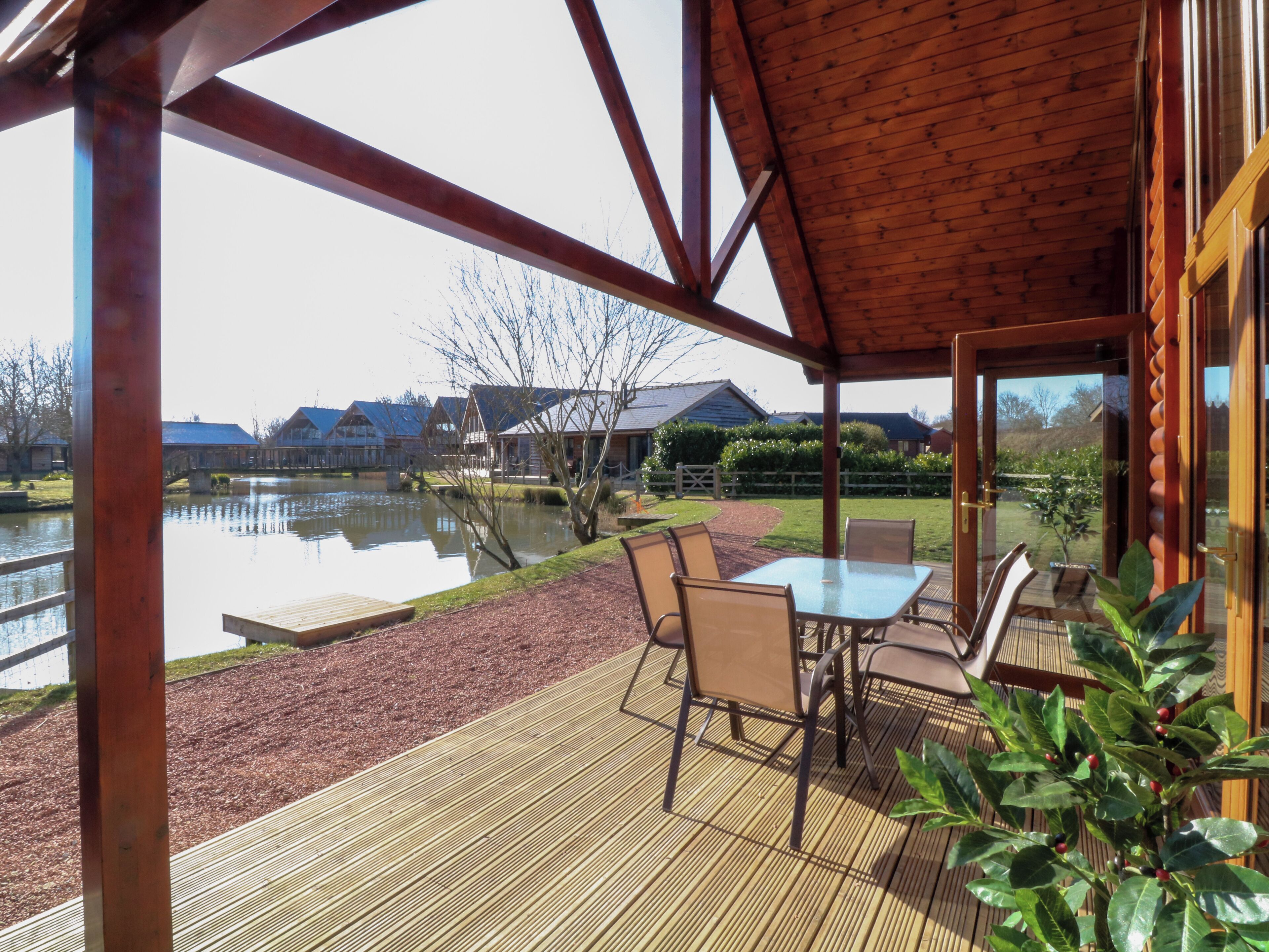 A covered outdoor area with a table and chairs, a wooden deck, and a view of a lake and buildings in the background.