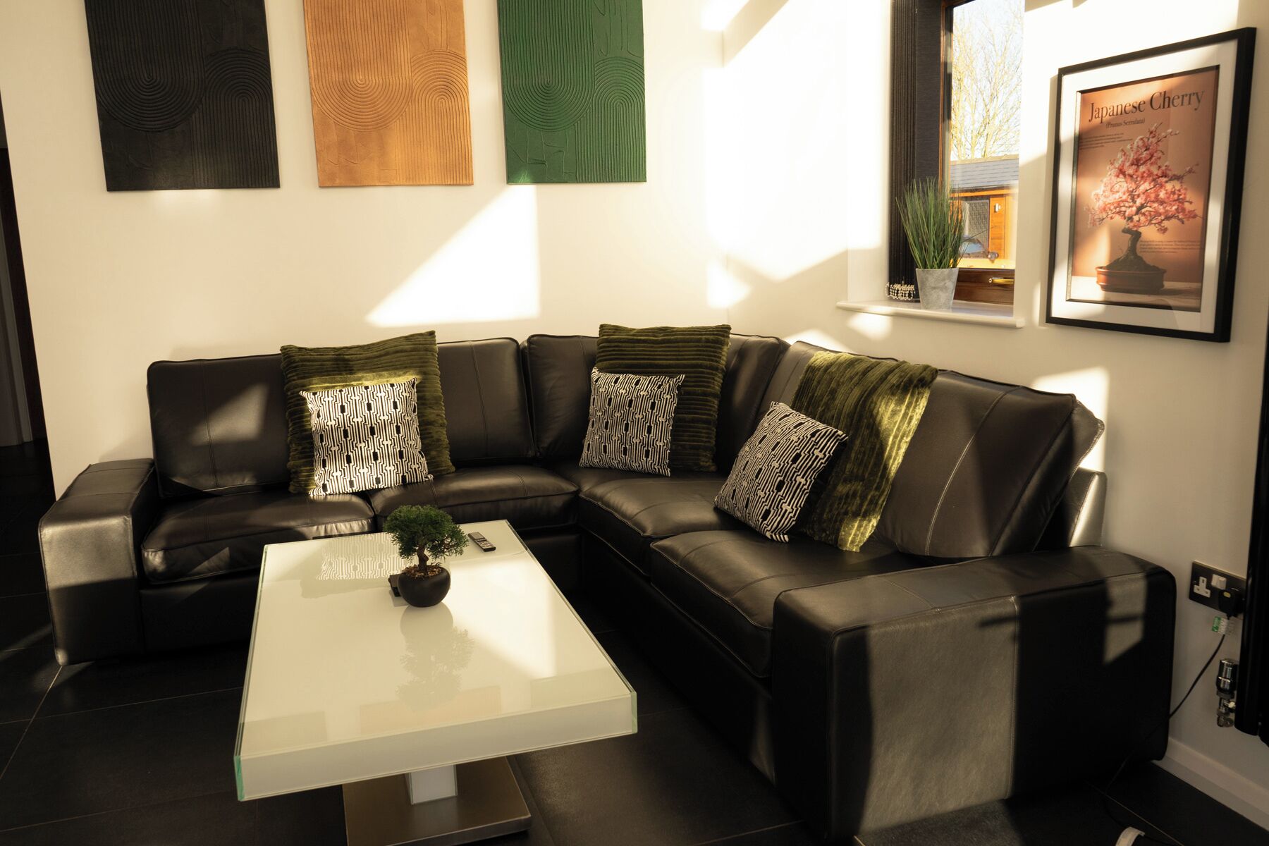 A modern living room with a black leather sofa, a glass coffee table, and patterned throw pillows.