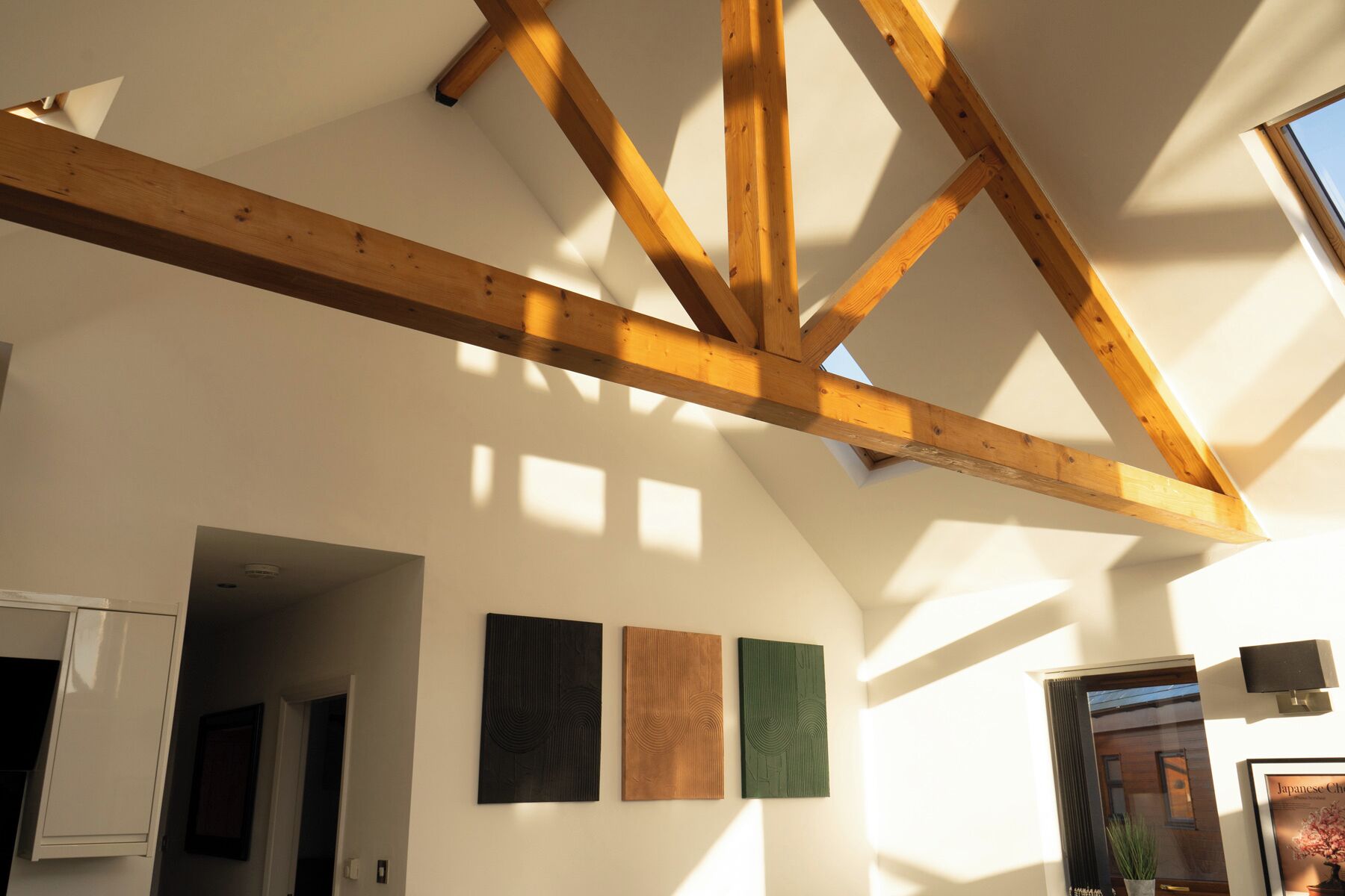 A room with exposed wooden beams, a skylight, and three framed artworks on the wall.
