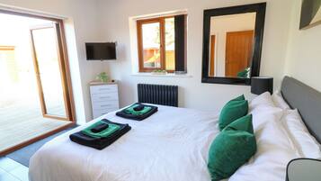 A bedroom with a bed, green pillows, a flat-screen TV, a window, and a radiator.