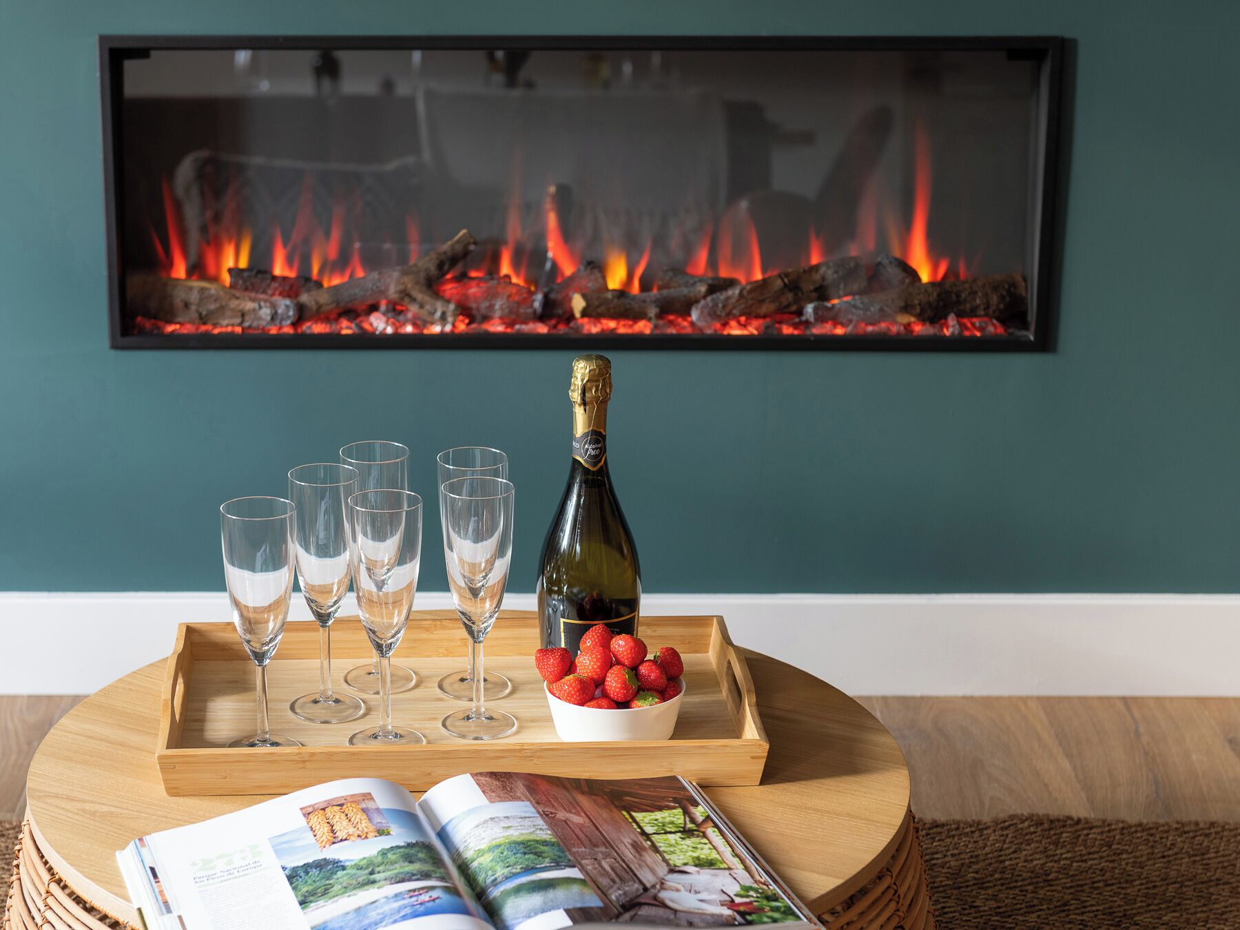 Een kamer met een open haard, een champagnefles, glazen, aardbeien en tijdschriften.