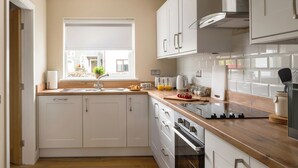 Een moderne keuken met witte kasten, een houten aanrecht, een inbouwoven en een raam met uitzicht op de straat.