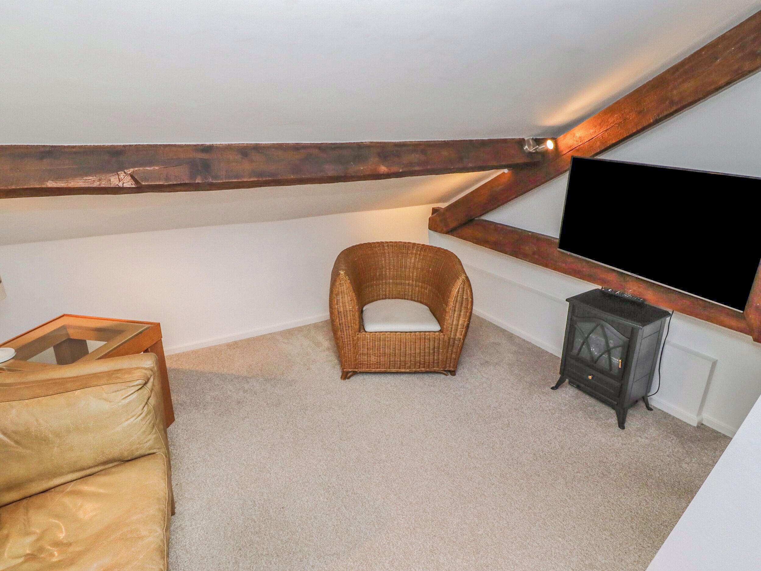 A cozy attic room with a wicker chair, a leather sofa, a flat-screen TV, and a small heater.