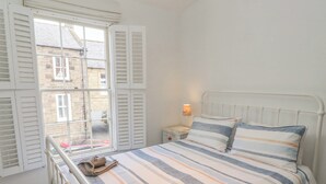 Une chambre à coucher avec un lit, une table de chevet, une lampe et une fenêtre avec des volets.
