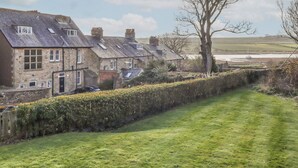 Une rangée de maisons en pierre aux toits inclinés, un sentier herbeux et un arbre au premier plan.