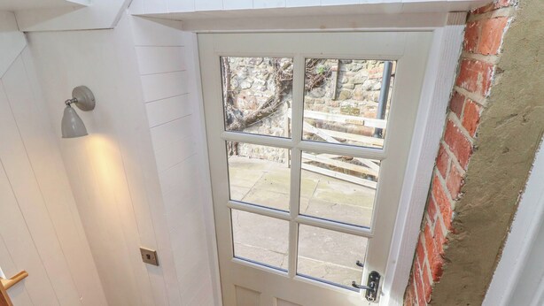 Une porte blanche avec un panneau de verre, un luminaire au-dessus, et un mur de briques sur la droite.