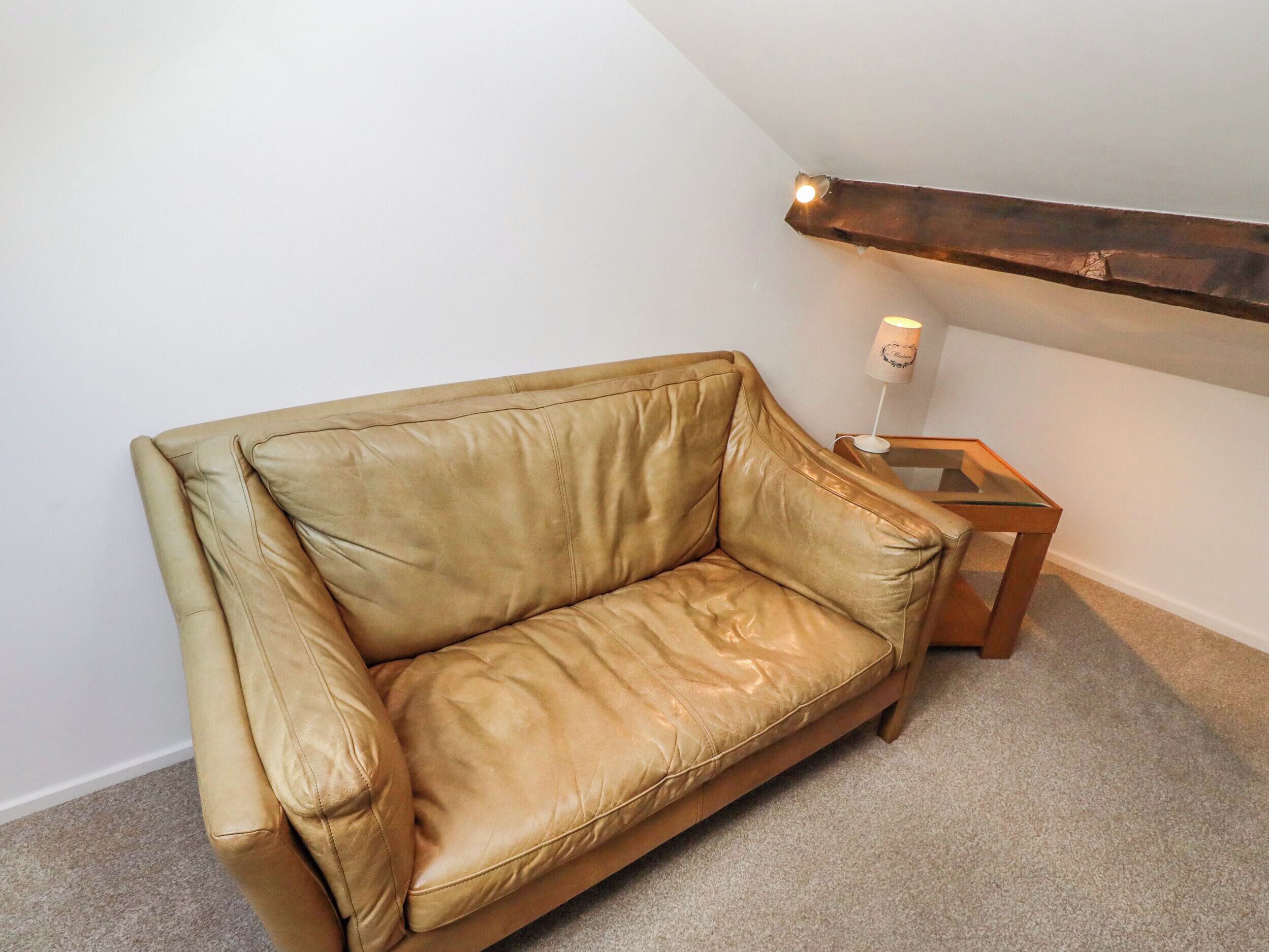 A tan leather sofa in a corner of a room with a wooden beam ceiling and a small wooden table beside it.
