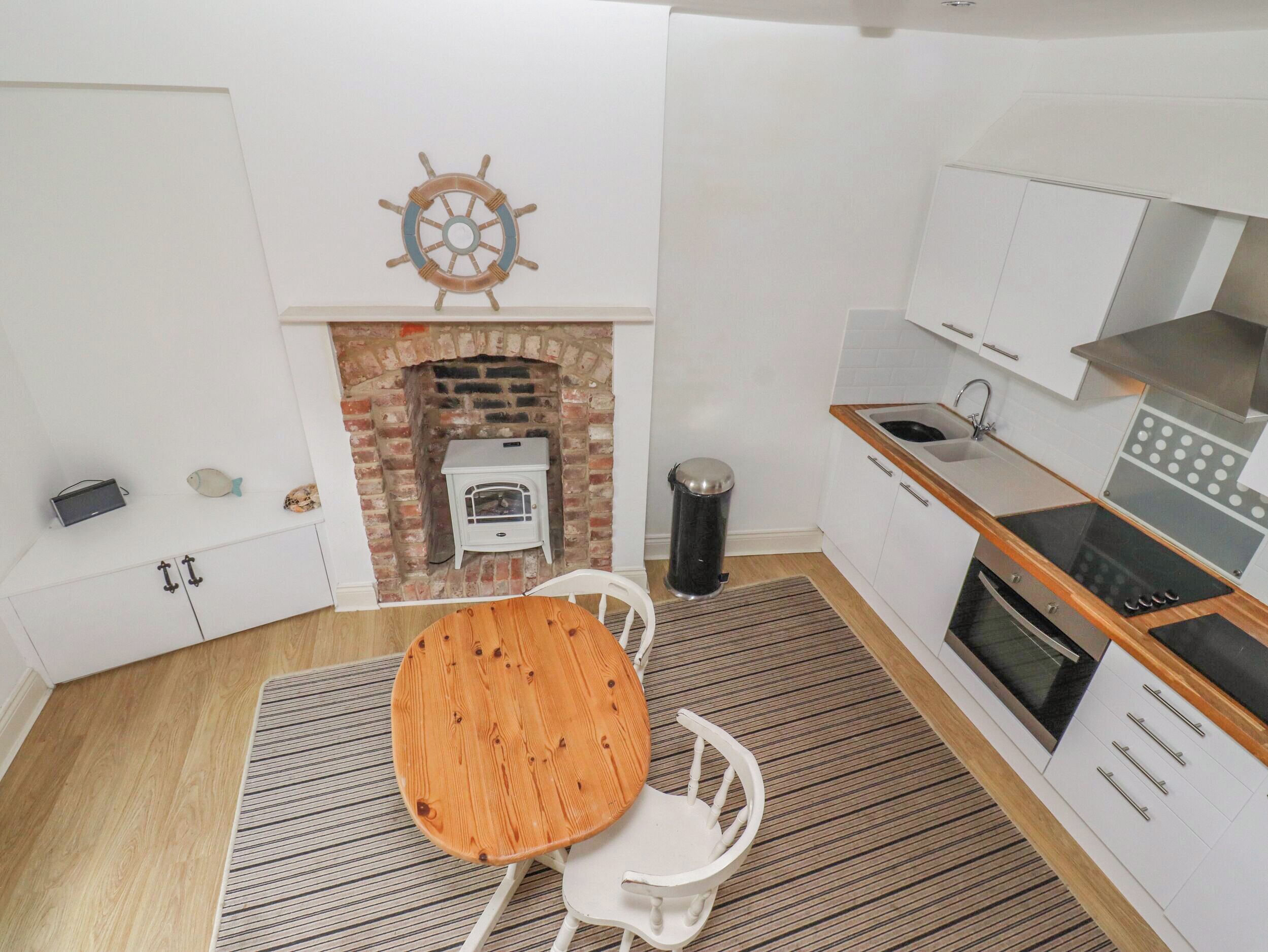 A compact kitchen with a brick fireplace, white cabinetry, a wooden table, and a white chair.