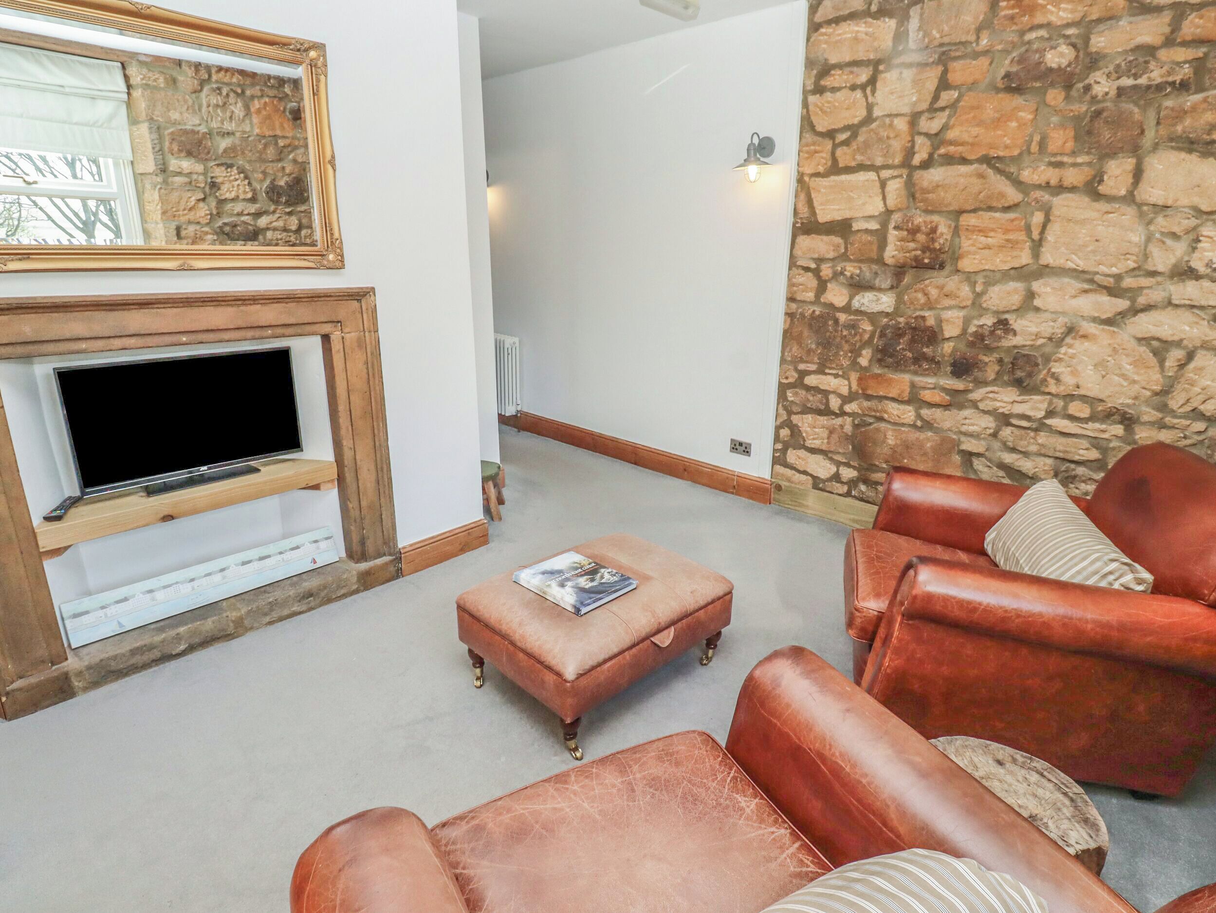 A living room with a fireplace, stone wall, leather sofas, and a television.