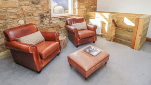 A cozy room with stone walls, two leather armchairs, a wooden bench, and a small ottoman with a magazine. - Seafield Granary (Alnwick)