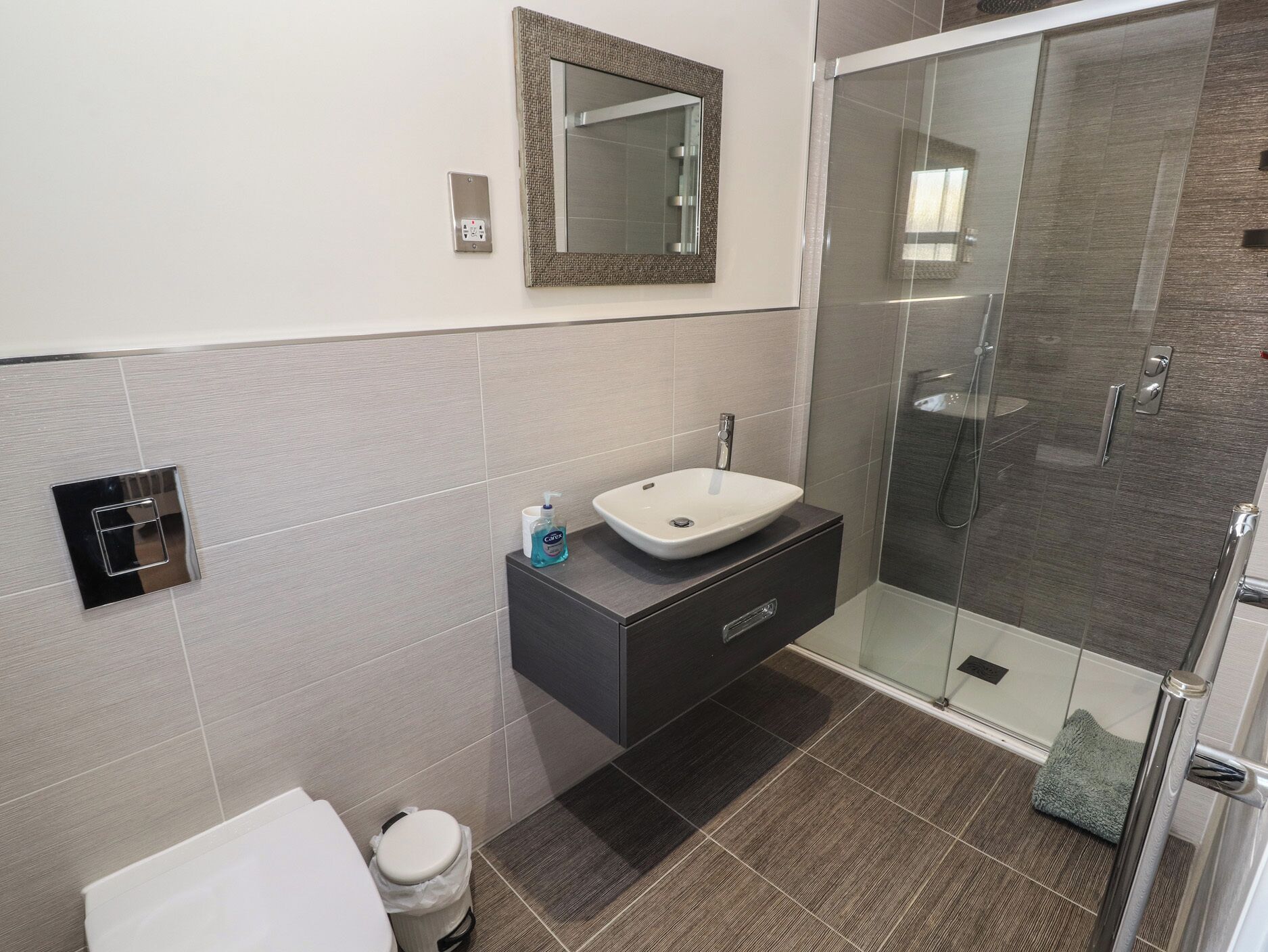 A modern bathroom with a glass shower enclosure, a white sink, and a dark vanity.