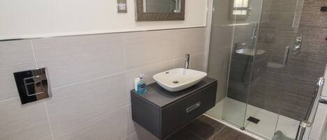 A modern bathroom with a glass shower enclosure, a white sink, and a dark vanity.