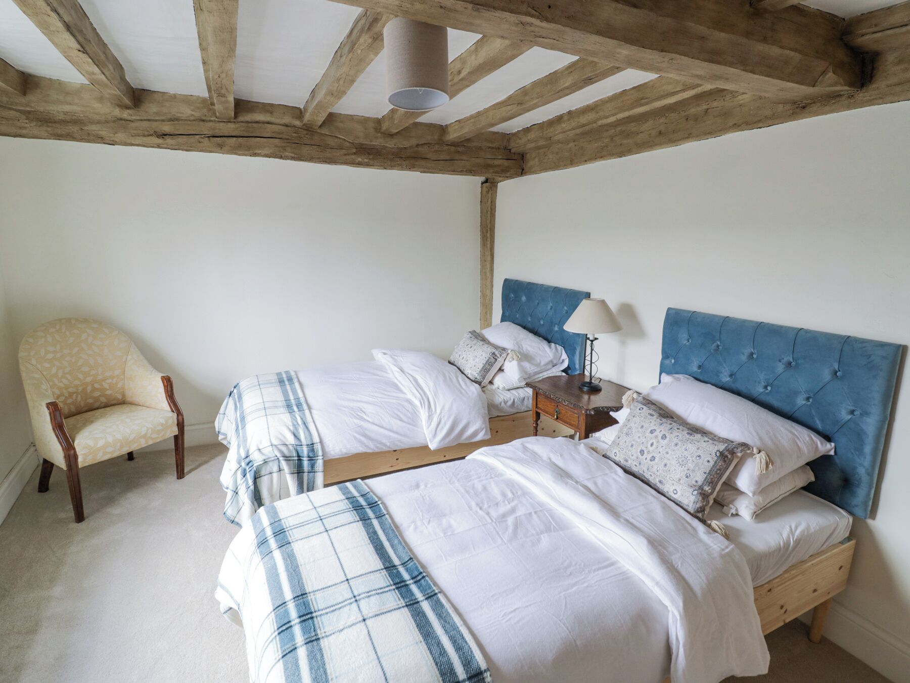 A bedroom with two beds, a chair, and a wooden ceiling structure.