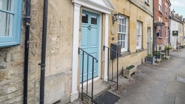 A traditional building with a blue door, stone walls, and a small porch with steps. - Lower Pack Horse Cottage (Cheltenham)