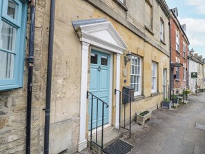 A traditional building with a blue door, stone walls, and a small porch with steps. - Lower Pack Horse Cottage (Cheltenham)