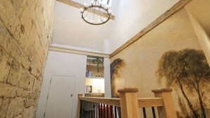 A high-ceilinged room with exposed brick walls, a wooden staircase, and a large painting. - Lower Pack Horse Cottage (Cheltenham)