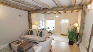 A cozy living room with a sofa, armchairs, and a coffee table. There is a wooden ceiling and a door leading to another room. - Lower Pack Horse Cottage (Cheltenham)