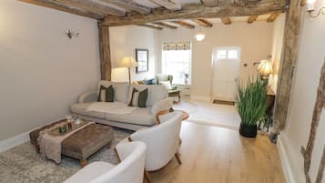 Un salon chaleureux avec un canapé, des fauteuils et une table basse. Le plafond est en bois et une porte donne accès à une autre pièce.