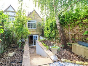 A stone house with a garden, a wooden fence, and a pathway leading to the entrance. - Lower Pack Horse Cottage (Cheltenham)