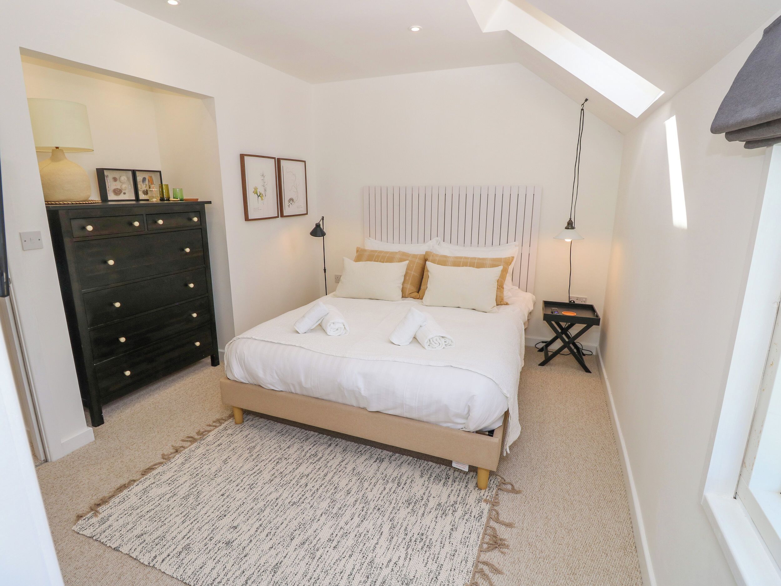 A bedroom with a bed, a dresser, a nightstand, and a skylight.