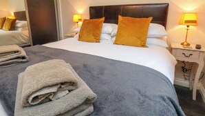 A neatly made bed with a grey blanket and two orange pillows, a bedside lamp, and a folded towel on the floor. - Cowslip (Saltburn-by-the-Sea)